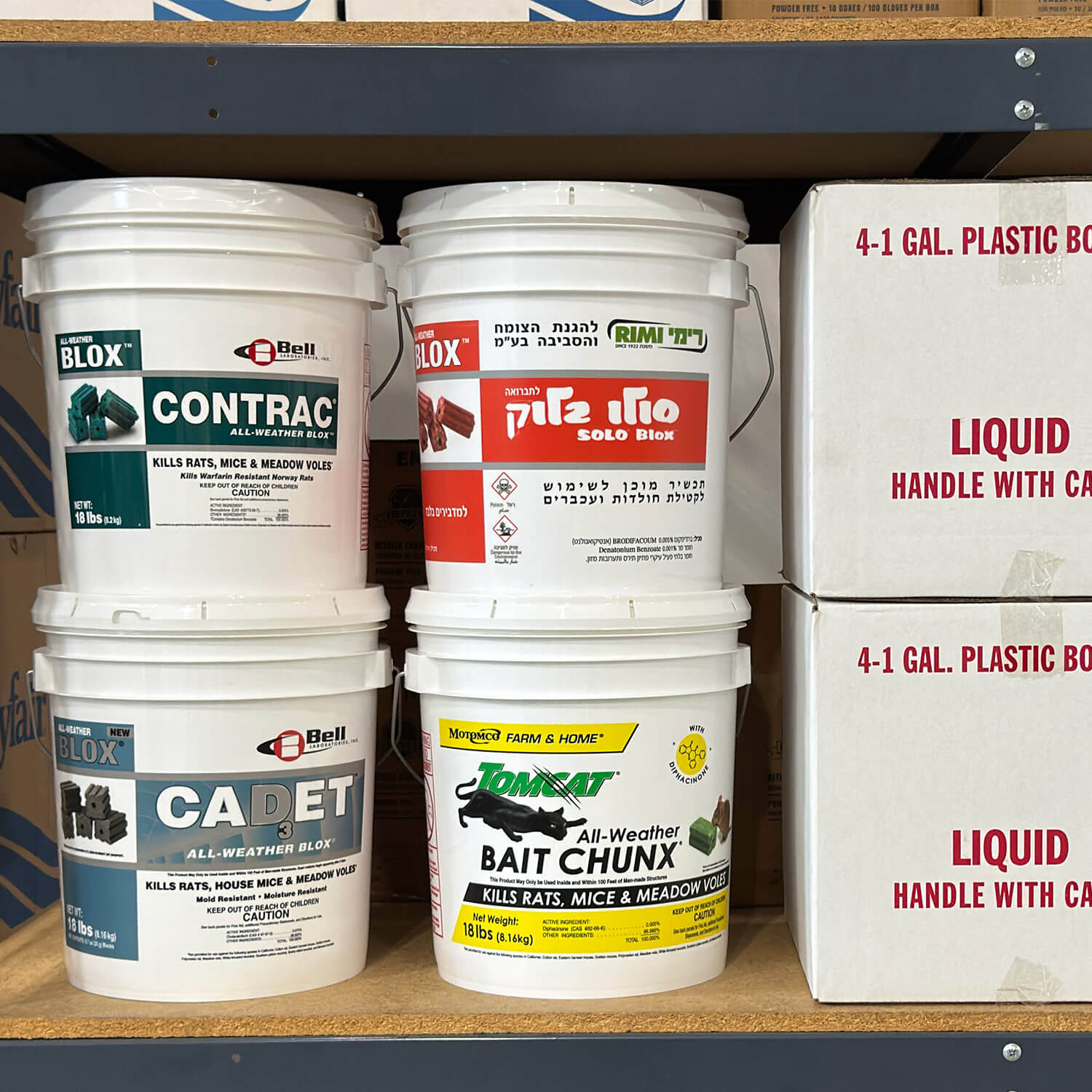 Stacked rodent bait pails from Bell Laboratories and Tomcat, including a Hebrew-language Solo Blox pail, with pail labels on a warehouse shelf