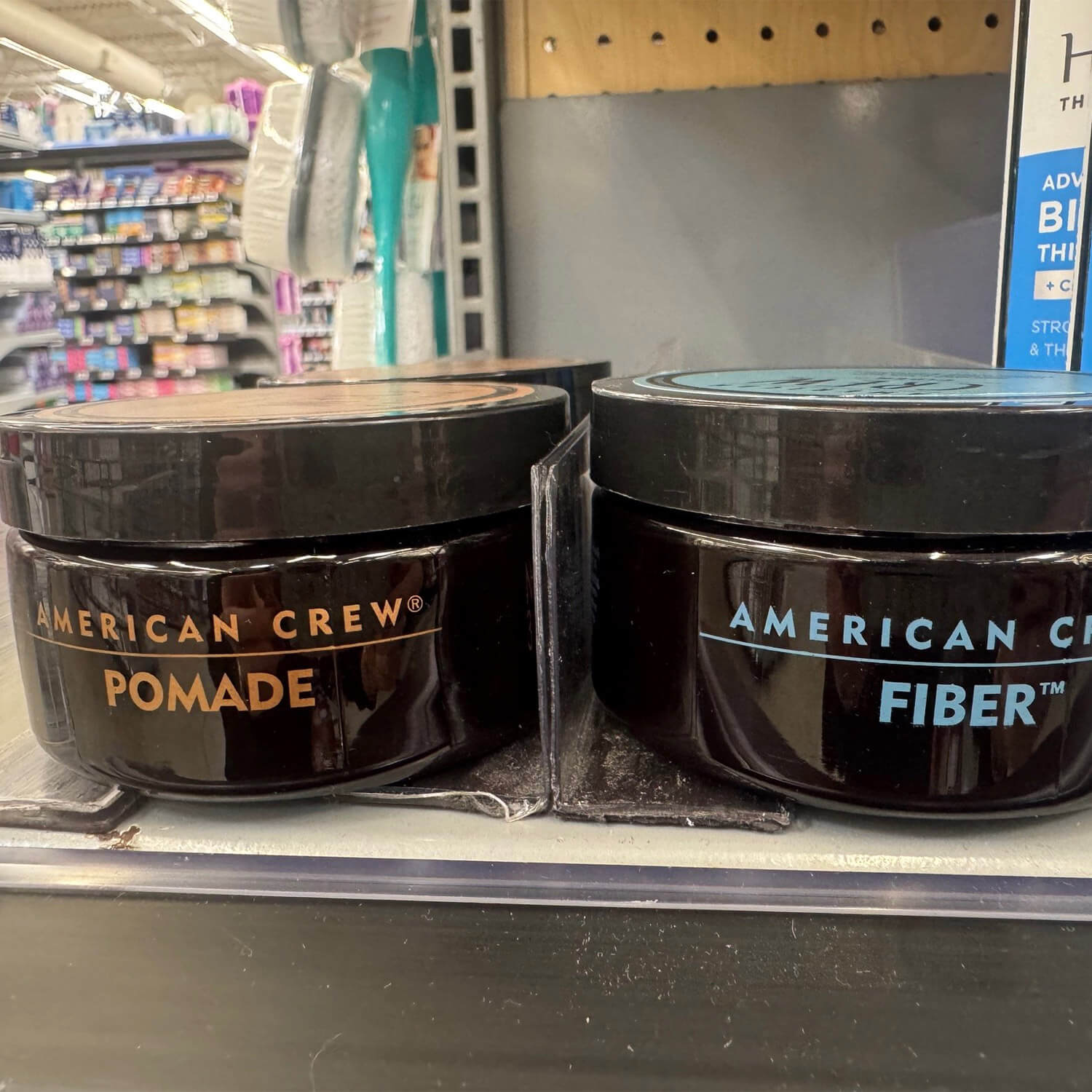 American Crew Pomade and Fiber jars with screen-printed metallic and blue lettering on a store shelf
