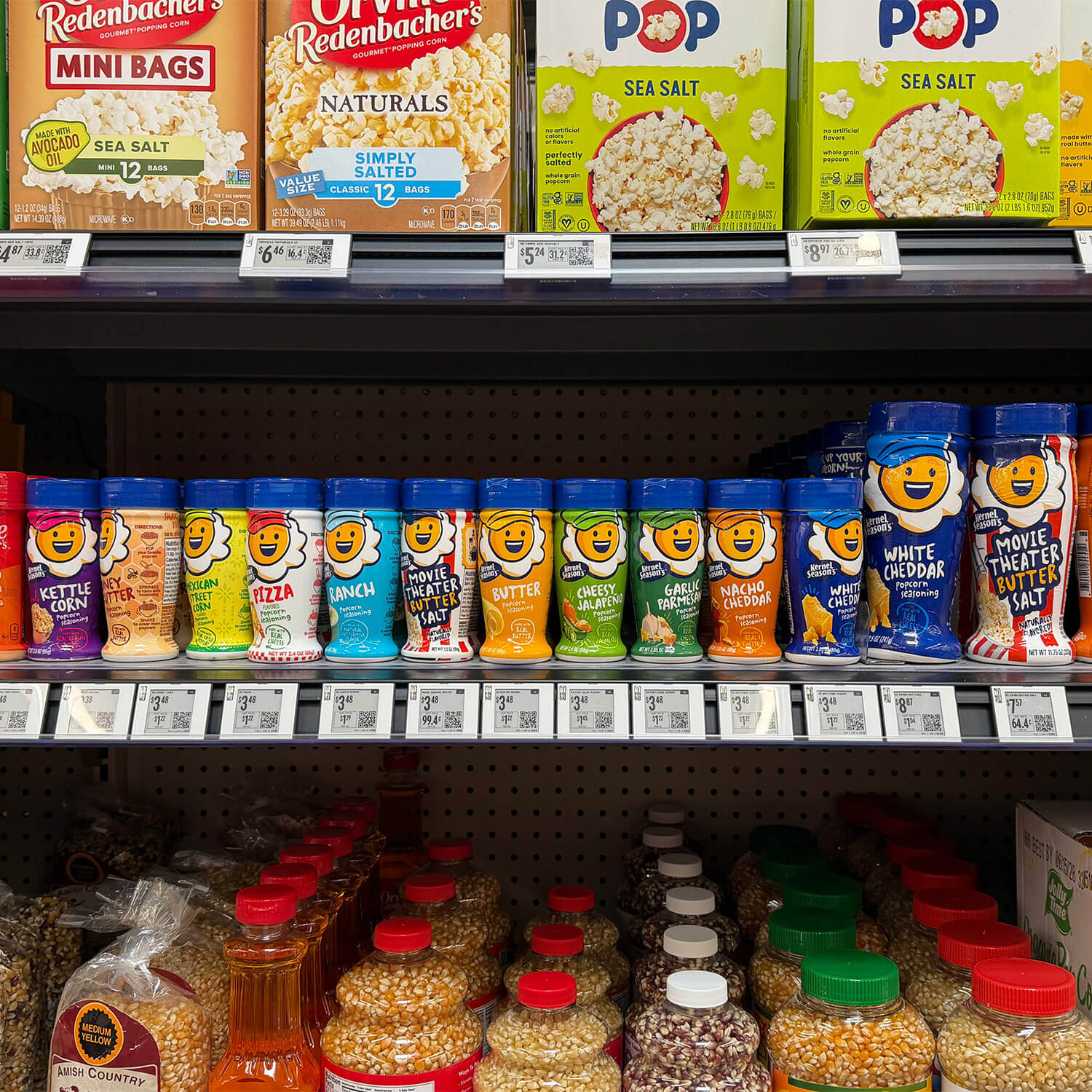 A row of Kernel Season’s popcorn seasoning shakers with full-body shrink sleeves on a grocery shelf