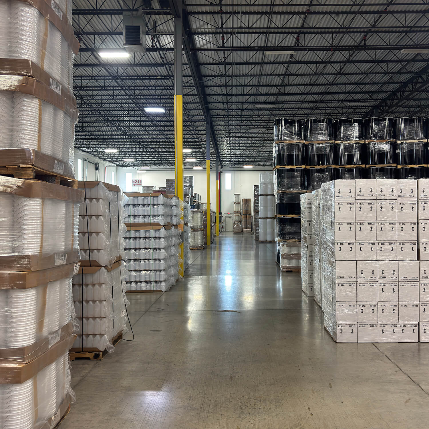 An ILLING warehouse aisle stocked with pallets of pails, gallon jugs, cased bottles, and drums
